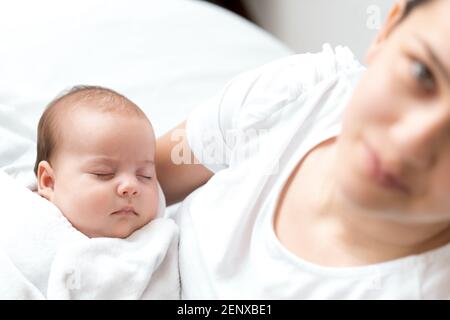 close-up portrait of mom with newborn baby on white background copy space. Young cute caucasian woman black haired holding child in arms motherhood