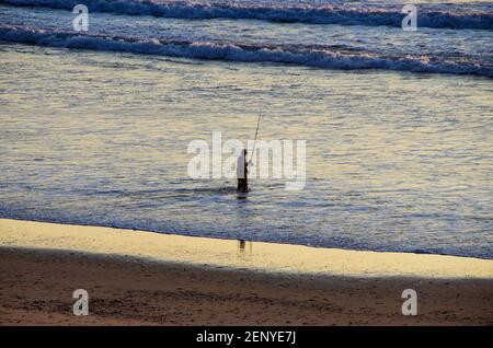 Fisherman in action. He stands in water and holds fly rod in one hand and  spoon in the other one. Also adult has a fishing net on the back. Green  Stock Photo - Alamy