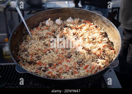 Cooking of traditional pilaf in big cauldron, street food in outdoor Stock Photo