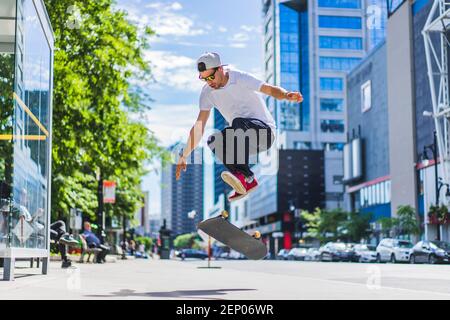Young skateboarder doing a flip trick on ground in downtown setting, Montreal, Quebec, Canada Stock Photo