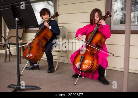 A boy holding cello looks on while his sister plays her instrument Stock Photo