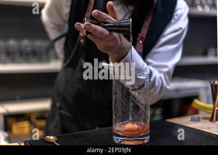 Barman in shirt and apron making an alcoholic drink with ice in a cocktail glass Stock Photo