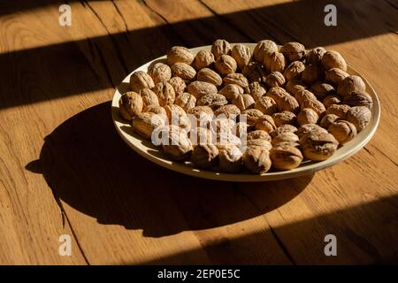 Plate of walnuts standing on a wooden table in a hard light Stock Photo