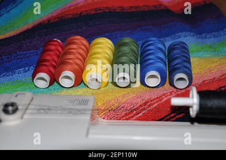 Sewing threads of the colors of the rainbow on the background of multicolored fabricc Stock Photo