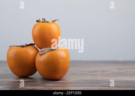 Three delicious fuyu persimmons placed on wooden table Stock Photo