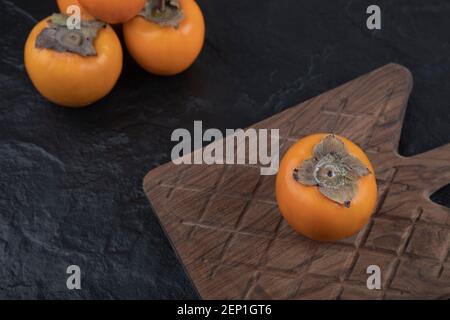 Single tasty fuyu persimmon on wooden cutting board Stock Photo