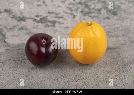 One whole purple plum with one whole lemon on stone background Stock Photo