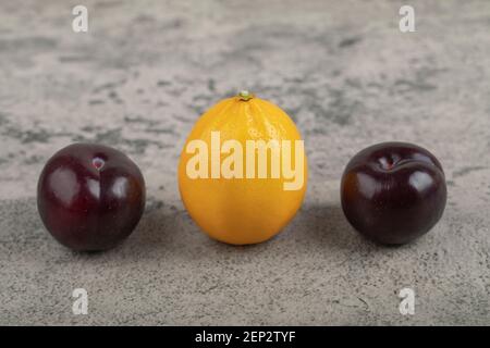 Two fresh purple plums with one whole lemon on stone background Stock Photo