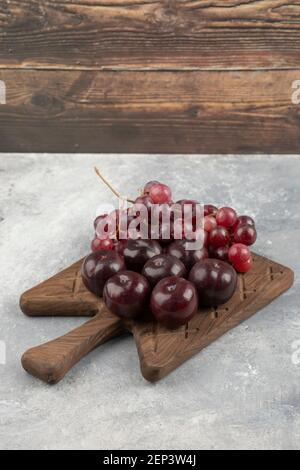 Wooden board of fresh red plums and grapes on marble surface Stock Photo