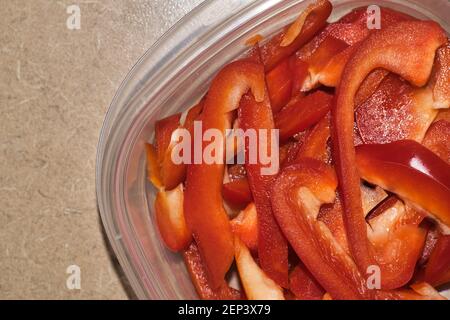 Sliced red bell peppers in a plastic container, partial overhead flat lay view. Stock Photo