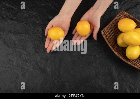 Female hands holding yellow lemons on black surface Stock Photo