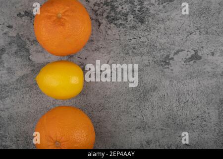 Two fresh orange fruits with whole lemon on stone table Stock Photo