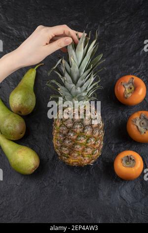 Female hand holding ripe pineapple on black surface Stock Photo