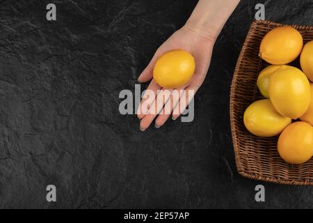 Female hand holding yellow lemon in her hand on black surface Stock Photo