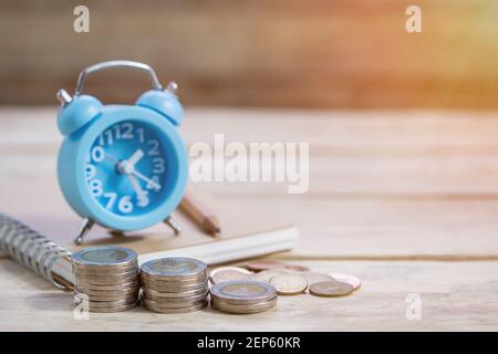 Coins,alram clock and pencil with empty notebook on wood table background. Office desk with money coins and business financial planning concept Stock Photo