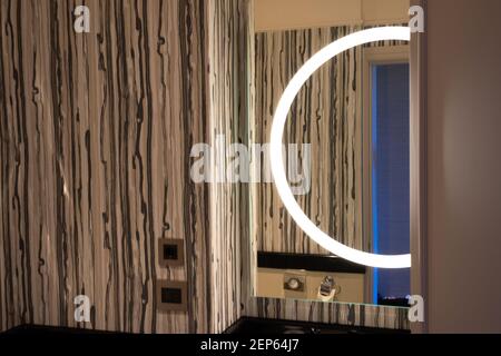 Modern bathroom decoration, including the space over the sink, round lamp reflected in the mirror, brown ornamental pattern on a wall Stock Photo