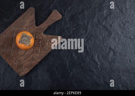 Single tasty fuyu persimmon on wooden cutting board Stock Photo