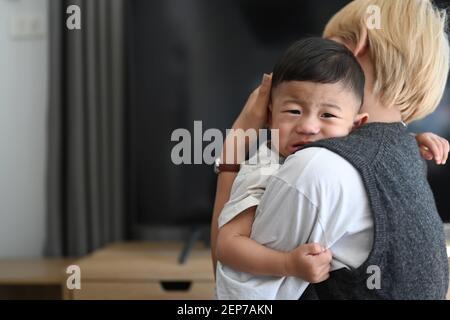 Image of Asian mother holding crying baby in comfortable home. Stock Photo