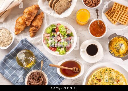 Broad assortment of food including omelette, croissants, salad, bread, oatmeal, jam, waffles, honey, choclate spread, coffee and orange juice served Stock Photo