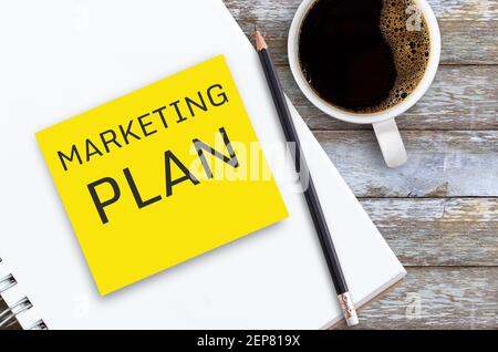 Business concept with text MARKETING PLAN on yellow post it sticky note with notebook,pencil and cup of coffee on office desk or wood table in workpla Stock Photo