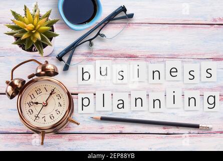 Business planning text on sticky notes and retro alarm clock,glasses,cup of coffee and flower on a wooden table. Photo in retro color image style. Top Stock Photo