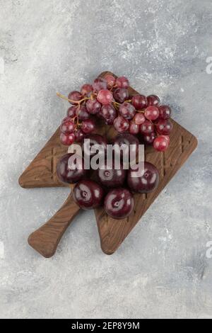 Wooden board of fresh red plums and grapes on marble surface Stock Photo