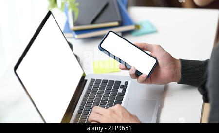 Cropped shot of young man using mobile phone getting message with confirmation making transaction on laptop computer. Stock Photo