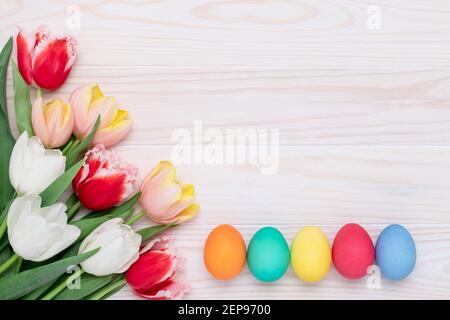 Painted Easter eggs and tulips on a wooden background, floral festive frame. Springtime, April. Celebration postcard, colorful mockup. Holiday layout Stock Photo