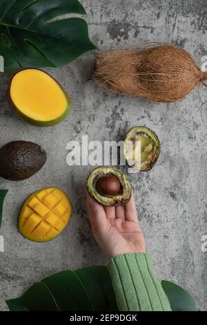 Female hand holding halved ripe avocado on marble surface Stock Photo