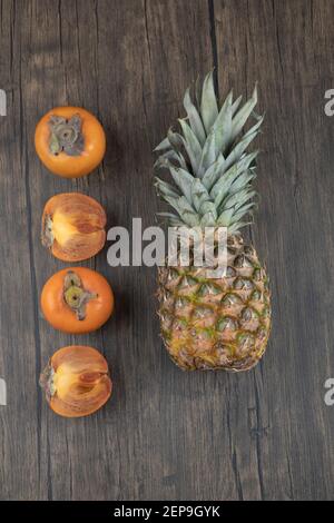 Sliced persimmon fruits and ripe pineapple on wooden surface Stock Photo