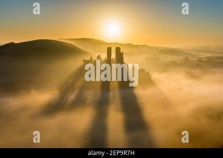 Corfe Castle, Dorset, UK.  27th February 2021.  UK Weather.  A spectacular sunrise with the shadows of the ruined towers on the mist surrounding Corfe Castle in Dorset on a cold frosty morning at dawn.  Picture Credit: Graham Hunt/Alamy Live News