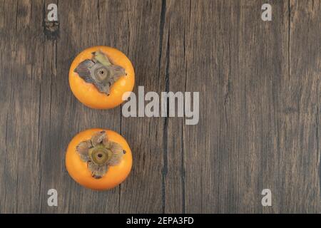 Two ripe persimmon fruits placed on wooden surface Stock Photo