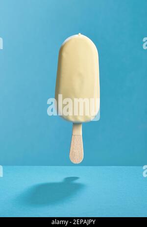 levitating ice cream covered with white chocolate on blue background Stock Photo