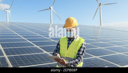 Man worker using digital tablet while wearing safety mask at renewable energy farm during coronavirus outbreak - Soft focus on face Stock Photo