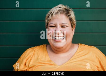 Portrait of curvy woman smiling on camera outdoors with green background - Focus on face