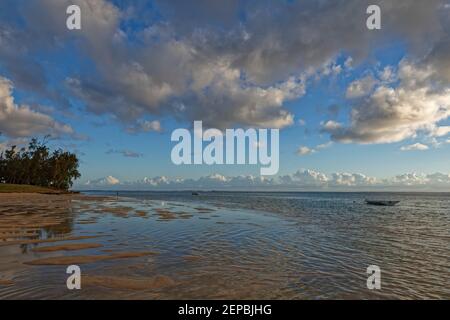 The Tide going out on the edge of Le Morne Beach, with small pools of water forming in the sand, and open Fishing boats moored in the lagoon. Stock Photo