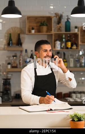 Portrait of a Happy young chef wearing uniform and kitchen gown in restaurant while talking by phone Stock Photo