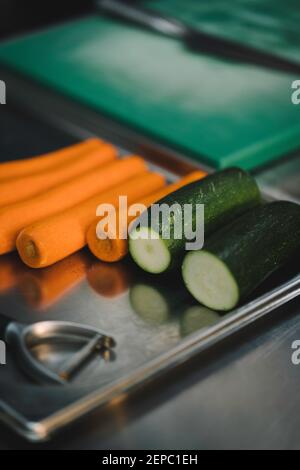 carrots and zucchini on stainless steel tray with peeler in restaurant kitchen. Stock Photo