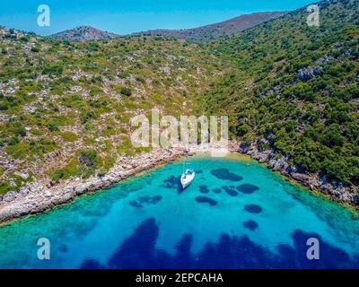 Aerial view of sailing boat anchored in turquoise color wonderful sea bay. Crystal clear water. Drone camera. Tranquility and emptiness. Picturesque