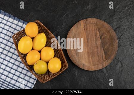 Wooden wicker basket of whole lemons and empty plate on black surface Stock Photo