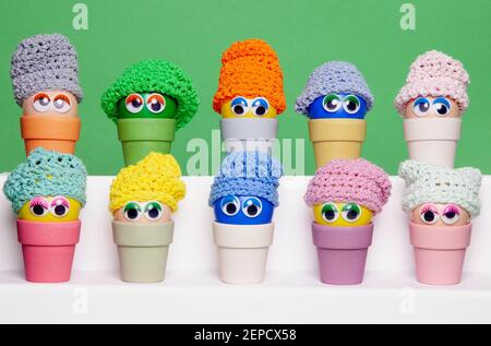 Colourful Easter eggs, made of recycled plastic, with wobbly eyes and colourful knitted hats, aligned horizontally and sitting in  bamboo egg holders Stock Photo