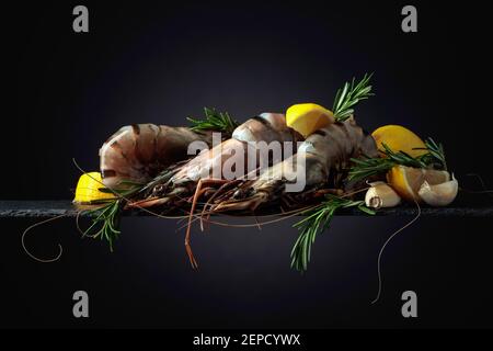 Fresh tiger prawns with lemon, rosemary, and garlic on a black background. Copy space. Stock Photo