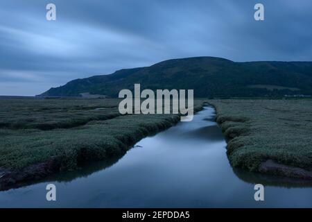 Water flowing through a salt marsh leading to Bossington Hill, Somerset. Stock Photo