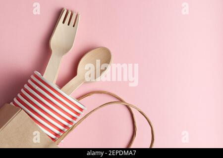eco-friendly and disposable kitchenware template. composition with wooden spoons, forks, paper cups, paper package at pink coral background. Stock Photo