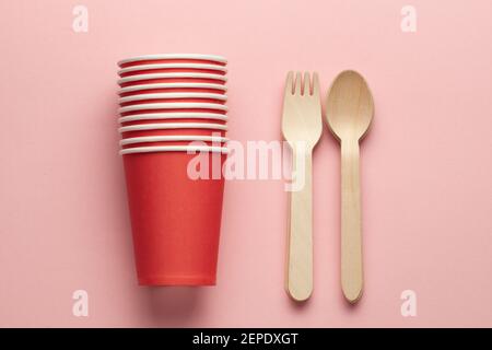 wooden forks and paper cup at pink coral background. eco-friendly and disposable kitchenware. flat lay. copy space. central composition Stock Photo