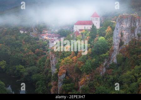 A misty foggy morning view of the medieval hilltop village of Saint-Cirq-Lapopie with autumn colours in the Lot Valley of southwest France Stock Photo