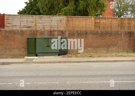 Road side green telecoms cabinet in front of brick wall & fence in Great Blakenham. A narrow & wide green cabinets in Great Blakenham Stock Photo