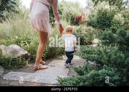 toddler learning to walk with the help of his mother outdoors Stock Photo