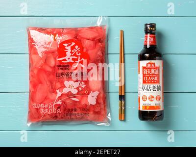 Varna, Bulgaria, February 25, 2021. Chinese pink pickled sliced ginger, mushroom soy sauce in a dark bottle and chopsticks on a blue wooden table. Stock Photo