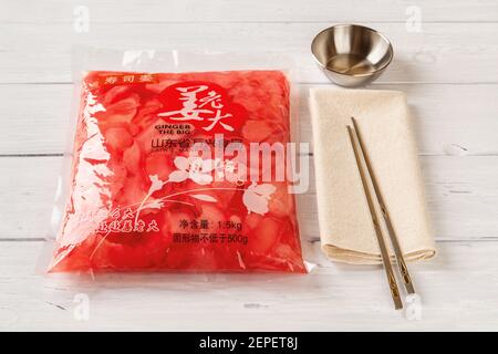 Varna, Bulgaria, February 25, 2021. Chinese pink sliced pickled ginger, metal sauce bowl and pair of chopsticks on a white wooden table. Stock Photo